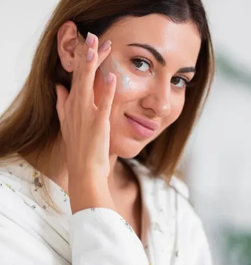 Mulher aplicando creme facial em frente ao espelho Mulher aplicando creme facial em frente ao espelho
